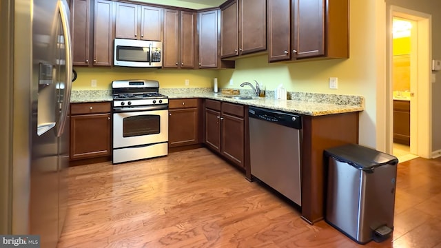 kitchen featuring light stone counters, appliances with stainless steel finishes, light hardwood / wood-style floors, and sink