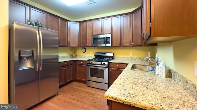 kitchen featuring sink, stainless steel appliances, light wood-type flooring, and light stone counters