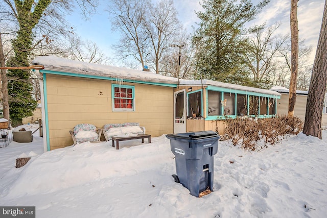 snow covered back of property featuring a sunroom