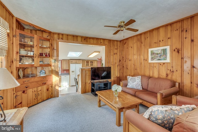 living room with ceiling fan, light colored carpet, wooden walls, and a skylight