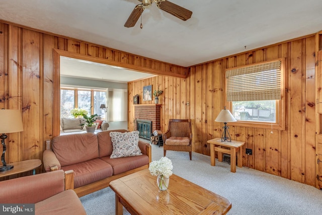 carpeted living room with ceiling fan, wooden walls, and a brick fireplace