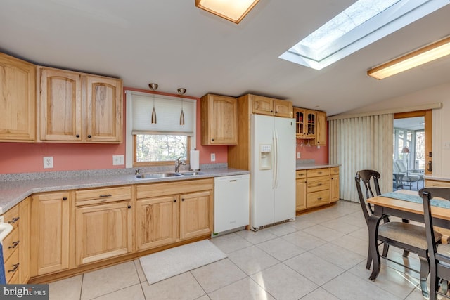 kitchen featuring light tile patterned floors, white appliances, vaulted ceiling with skylight, and sink