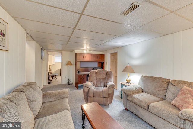 carpeted living room featuring a drop ceiling and wooden walls