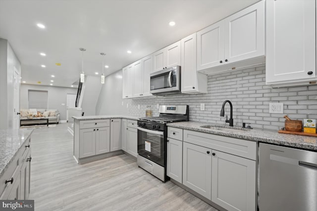 kitchen with light stone countertops, white cabinetry, sink, hanging light fixtures, and stainless steel appliances