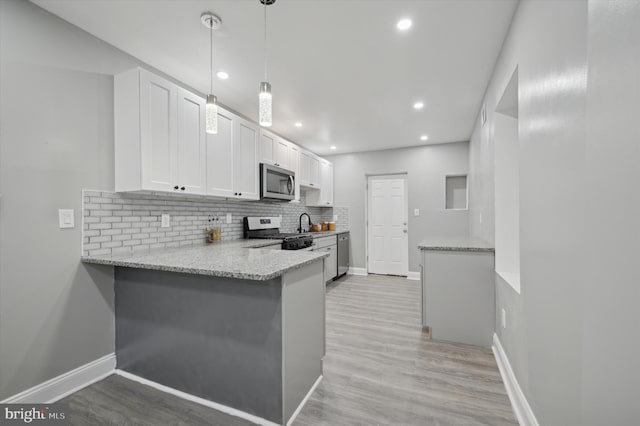 kitchen featuring kitchen peninsula, stainless steel appliances, pendant lighting, white cabinets, and light hardwood / wood-style floors