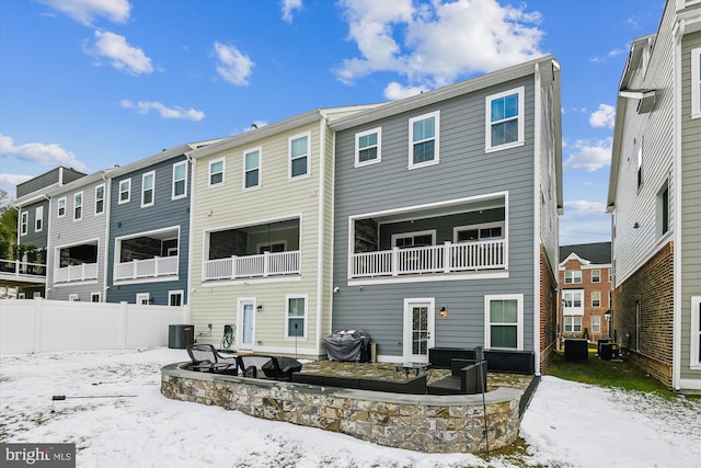 snow covered back of property featuring central AC unit and a balcony