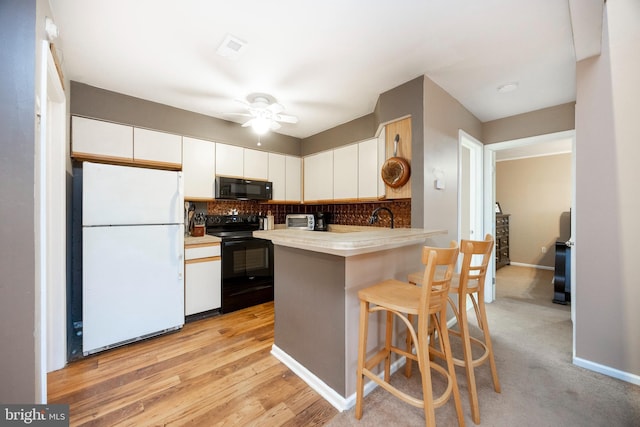 kitchen featuring white cabinetry, ceiling fan, a kitchen breakfast bar, kitchen peninsula, and black appliances