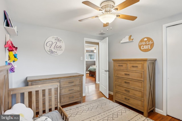 bedroom with ceiling fan, a nursery area, and light hardwood / wood-style floors