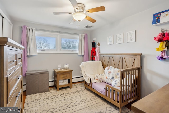 bedroom with a nursery area, baseboard heating, and ceiling fan