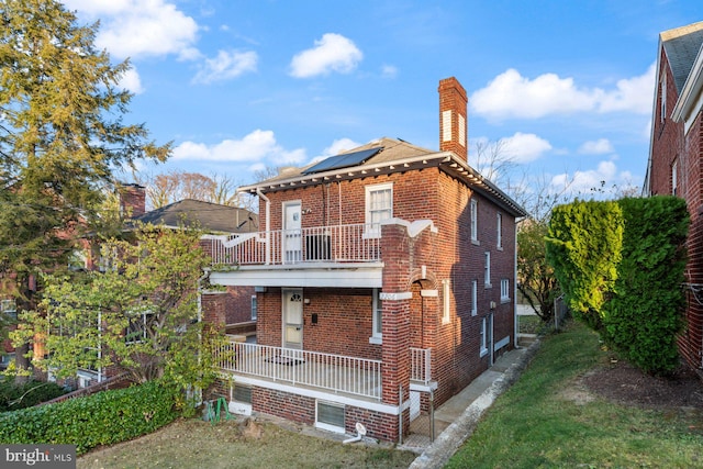 back of house with a yard, a balcony, and solar panels