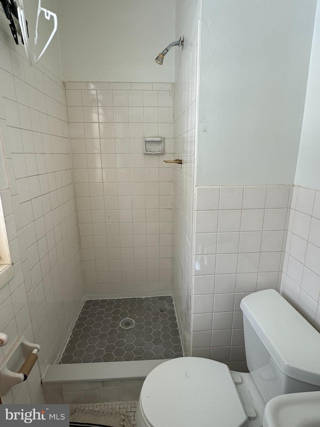 bathroom featuring tile patterned flooring, a tile shower, toilet, and tile walls