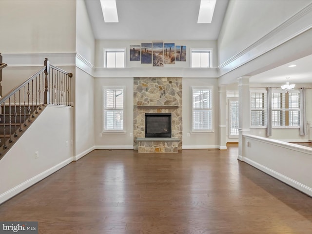 unfurnished living room with a skylight, a stone fireplace, high vaulted ceiling, dark hardwood / wood-style floors, and a notable chandelier