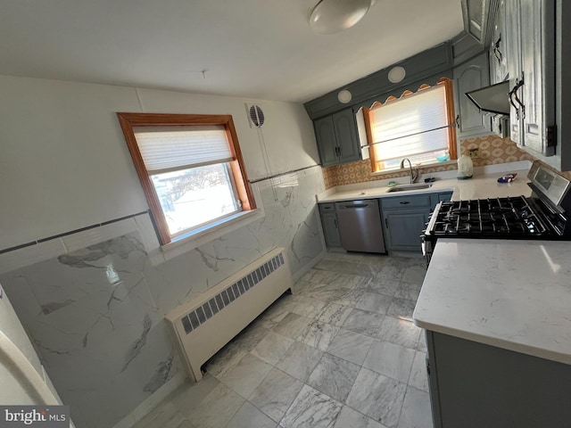 kitchen featuring stainless steel dishwasher, gray cabinetry, gas range oven, sink, and radiator heating unit