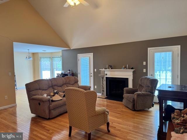 living room featuring light wood-type flooring, high vaulted ceiling, and ceiling fan with notable chandelier