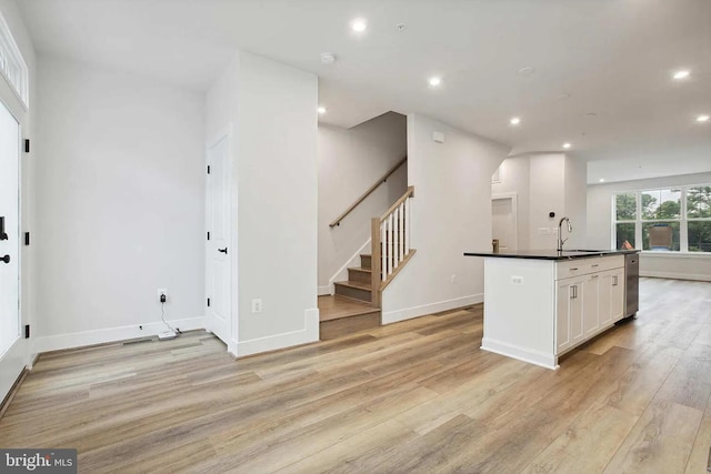 kitchen featuring white cabinets, light wood-type flooring, a center island with sink, and sink