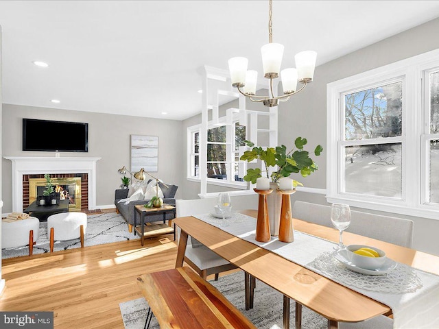 dining room with plenty of natural light, wood-type flooring, a chandelier, and a brick fireplace