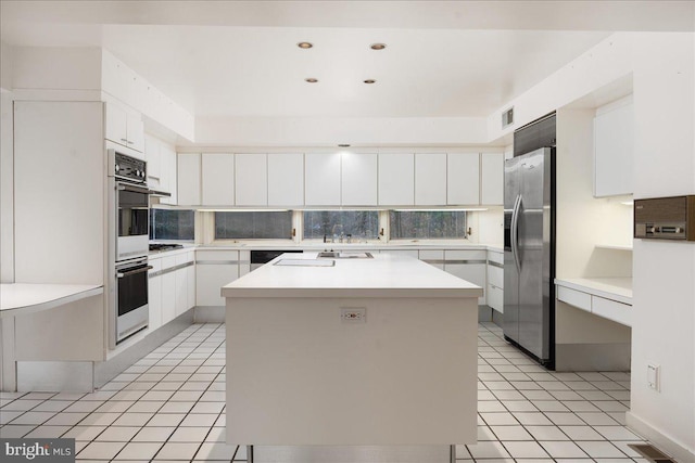 kitchen featuring a center island, stainless steel fridge, light tile patterned floors, tasteful backsplash, and white cabinets