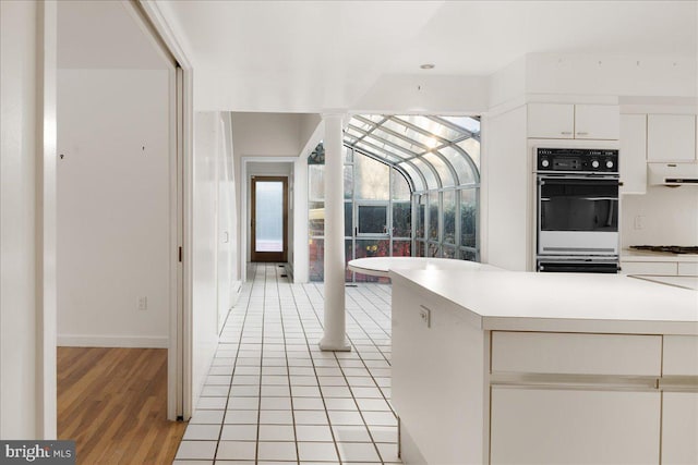 kitchen featuring white cabinetry, light tile patterned flooring, wall oven, and decorative columns