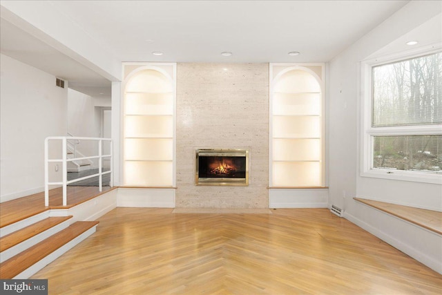 unfurnished living room featuring light hardwood / wood-style floors, a fireplace, built in shelves, and plenty of natural light