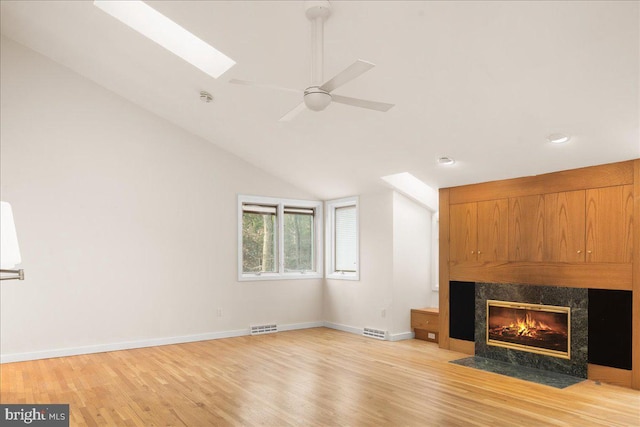 unfurnished living room featuring ceiling fan, light hardwood / wood-style floors, a high end fireplace, and vaulted ceiling with skylight