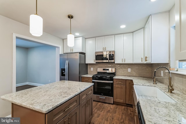 kitchen with white cabinetry, stainless steel appliances, backsplash, light stone countertops, and pendant lighting