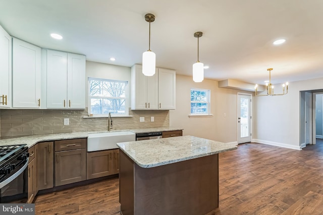 kitchen with tasteful backsplash, pendant lighting, white cabinets, light stone counters, and sink