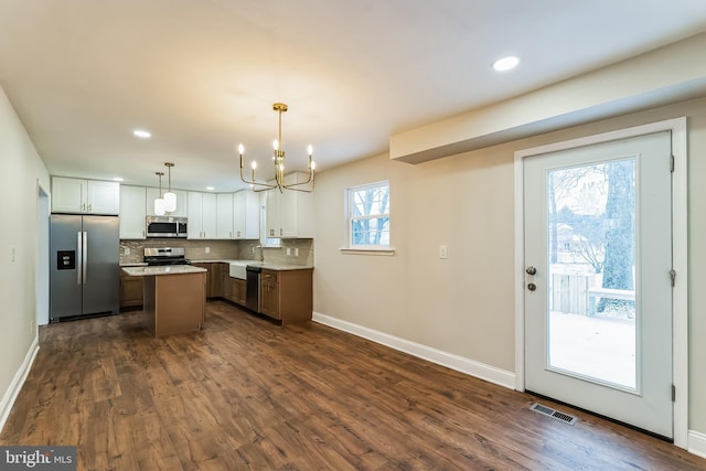 kitchen with appliances with stainless steel finishes, a kitchen island, pendant lighting, white cabinets, and sink