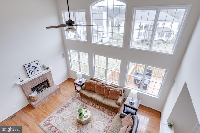 living room featuring wood finished floors, baseboards, visible vents, a fireplace, and ceiling fan