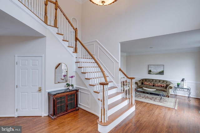 stairs featuring crown molding, wood finished floors, baseboards, and a towering ceiling