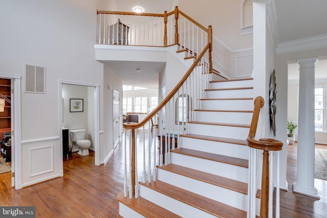 stairs with a high ceiling, wood finished floors, visible vents, and ornamental molding