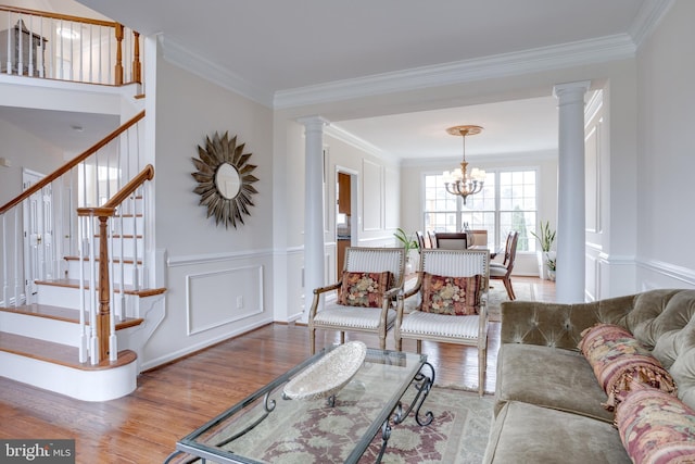 living room with stairway, wood finished floors, decorative columns, crown molding, and a notable chandelier