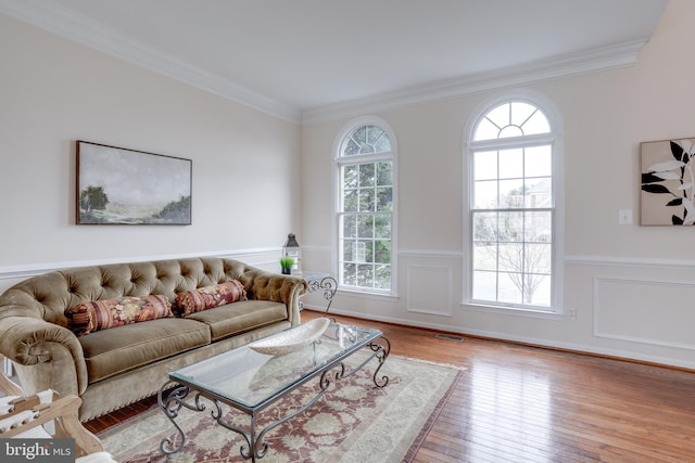 living area with a wainscoted wall, hardwood / wood-style flooring, visible vents, and ornamental molding