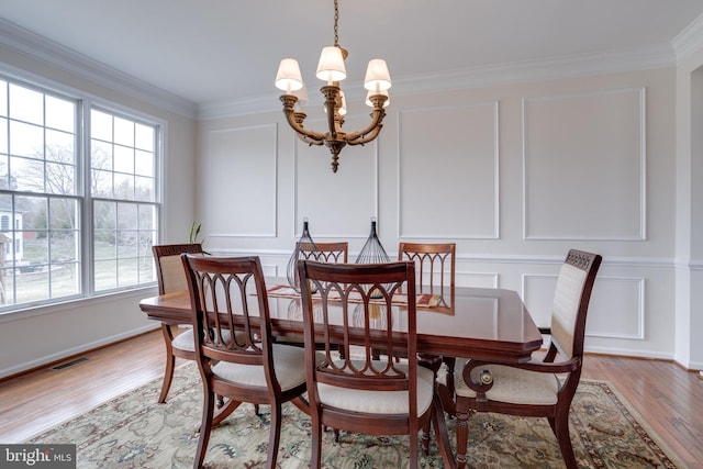 dining room with visible vents, light wood-style floors, an inviting chandelier, crown molding, and a decorative wall