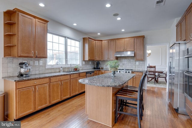 kitchen featuring light stone countertops, visible vents, a sink, under cabinet range hood, and light wood-type flooring