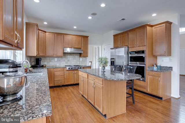 kitchen featuring light wood finished floors, a breakfast bar, stainless steel appliances, a sink, and under cabinet range hood