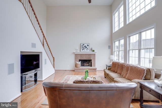 living area with visible vents, light wood-style floors, a fireplace, baseboards, and a towering ceiling