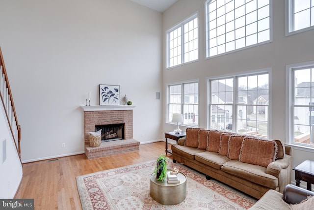 living room with stairway, light wood finished floors, baseboards, a brick fireplace, and a towering ceiling