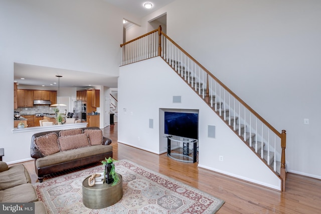 living area with stairway, baseboards, wood finished floors, and a towering ceiling