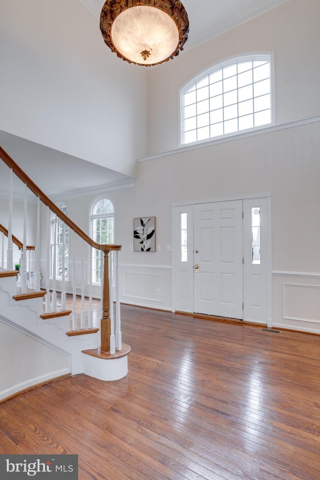 entryway with stairway, ornamental molding, wood-type flooring, wainscoting, and a decorative wall