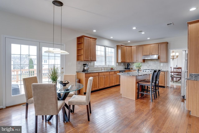 kitchen featuring light wood-type flooring, a kitchen island, open shelves, under cabinet range hood, and tasteful backsplash