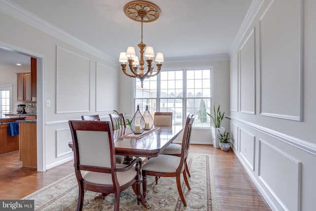 dining area with a decorative wall, light wood-style floors, an inviting chandelier, and ornamental molding