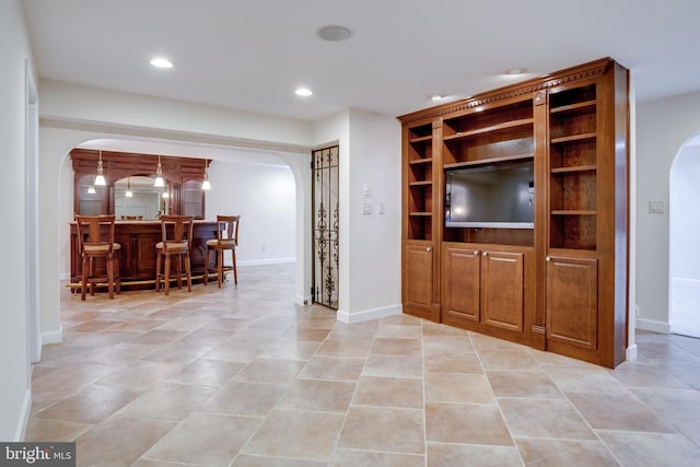 unfurnished living room featuring arched walkways, recessed lighting, a dry bar, and baseboards