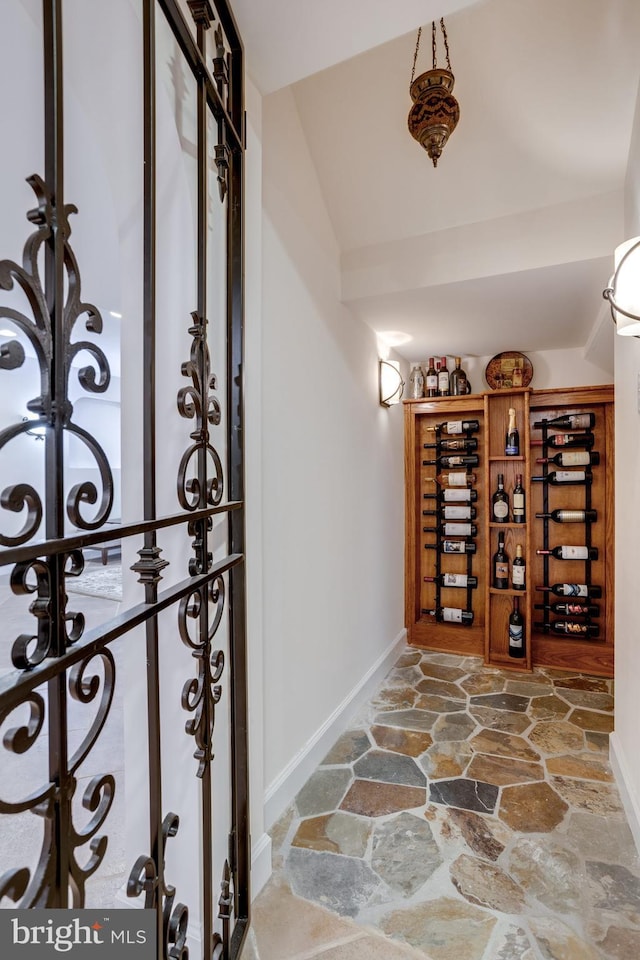 wine cellar featuring baseboards, stone tile floors, and vaulted ceiling