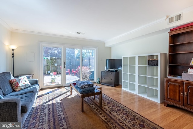 living area featuring light wood-style flooring, ornamental molding, and visible vents