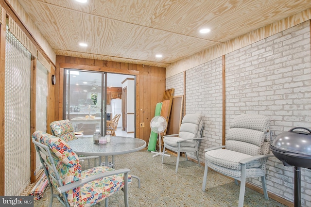 living area with wooden walls, brick wall, and wooden ceiling