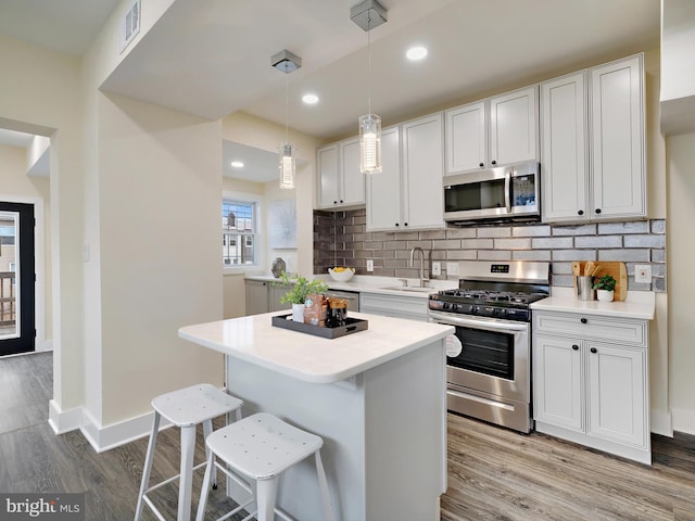 kitchen with sink, white cabinetry, hanging light fixtures, a kitchen breakfast bar, and stainless steel appliances