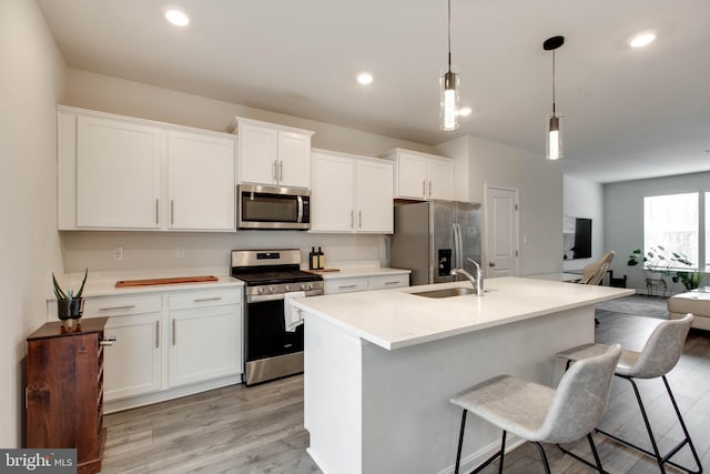 kitchen featuring decorative light fixtures, white cabinets, appliances with stainless steel finishes, and a kitchen island with sink