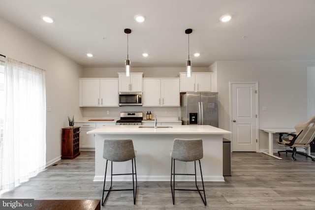 kitchen featuring decorative light fixtures, white cabinetry, stainless steel appliances, and a center island with sink