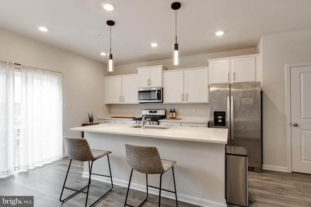 kitchen featuring a center island with sink, sink, hardwood / wood-style flooring, appliances with stainless steel finishes, and white cabinets