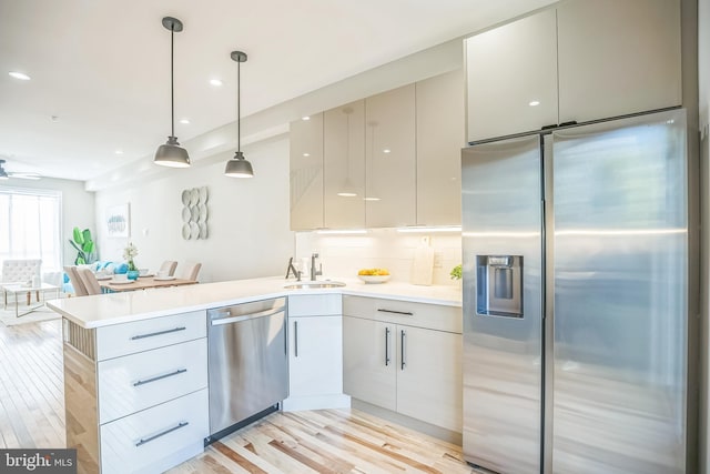 kitchen with decorative backsplash, appliances with stainless steel finishes, sink, pendant lighting, and light hardwood / wood-style floors